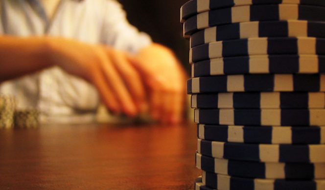 Casinos chips on a table and the player's hands with playing cards in a background