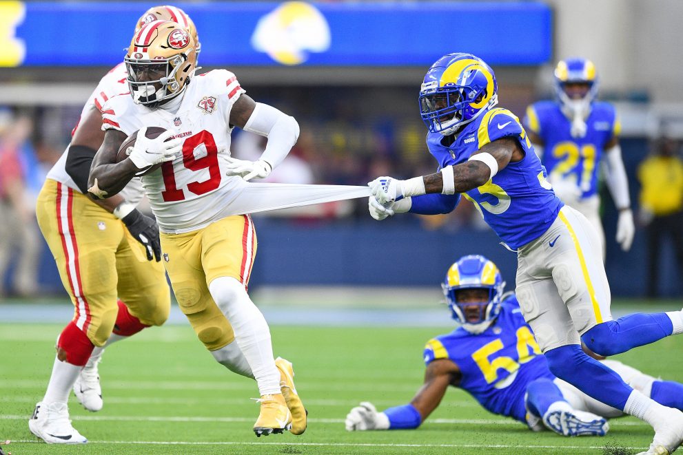 American football player runs after a catch as a player of opposite team pulls on his jersey during a game