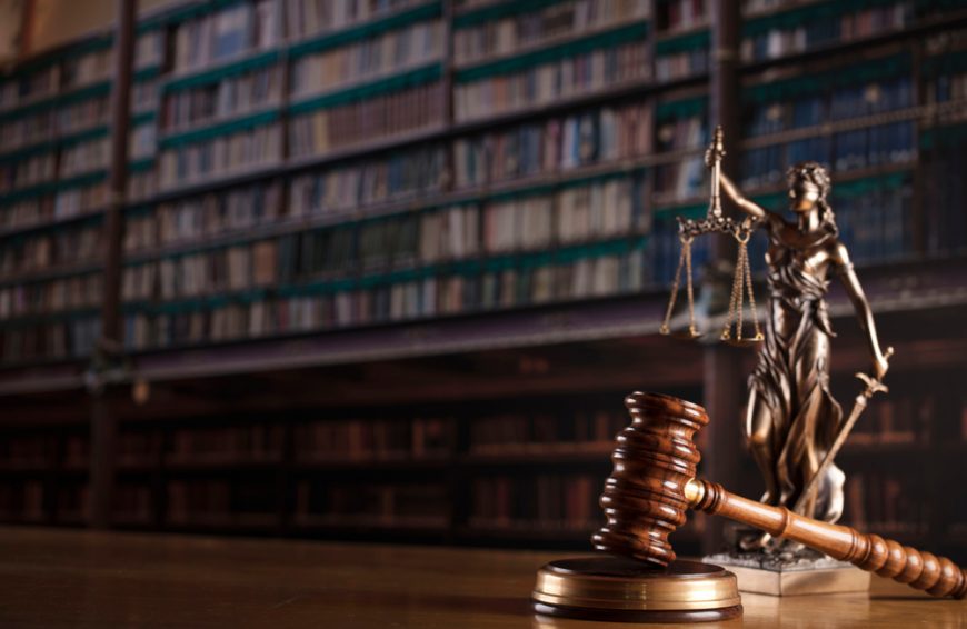 Judge’s gavel statue and scales of justice. Old courtroom library. Wooden desk