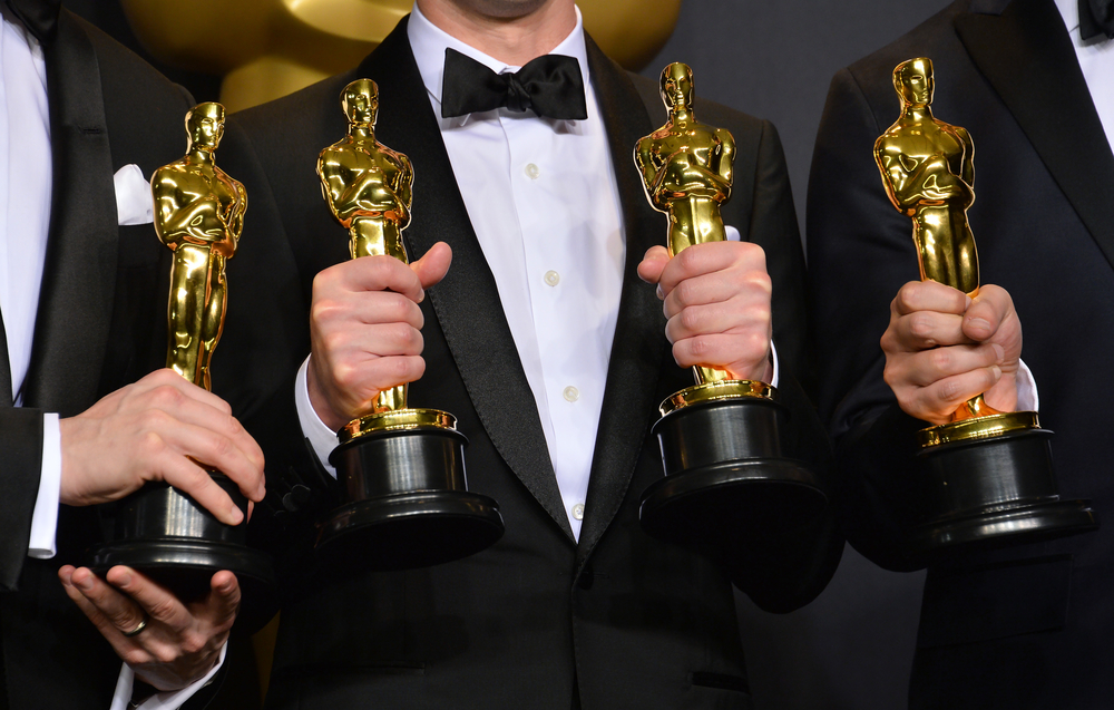 Four Oscar statues in hands of men wearing black suits