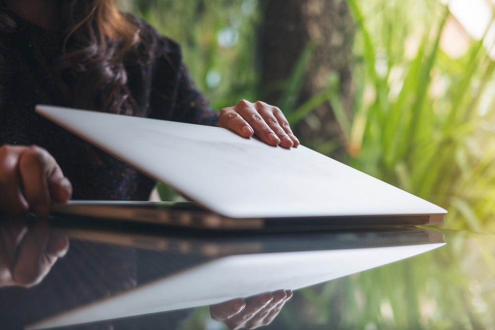 Closeup image of a businesswoman's hands close and open laptop on glass table in office with blur green nature background