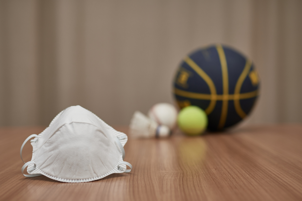 A mask in the foreground, and in the background different types of balls of different olympic sports