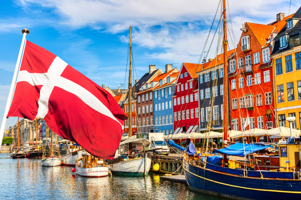 Famous old Nyhavn port in the center of Copenhagen, Denmark during summer sunny day with Denmark flag on the foreground.