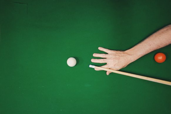 Red and white balls on a pool table and a hand with a cue ready to hit