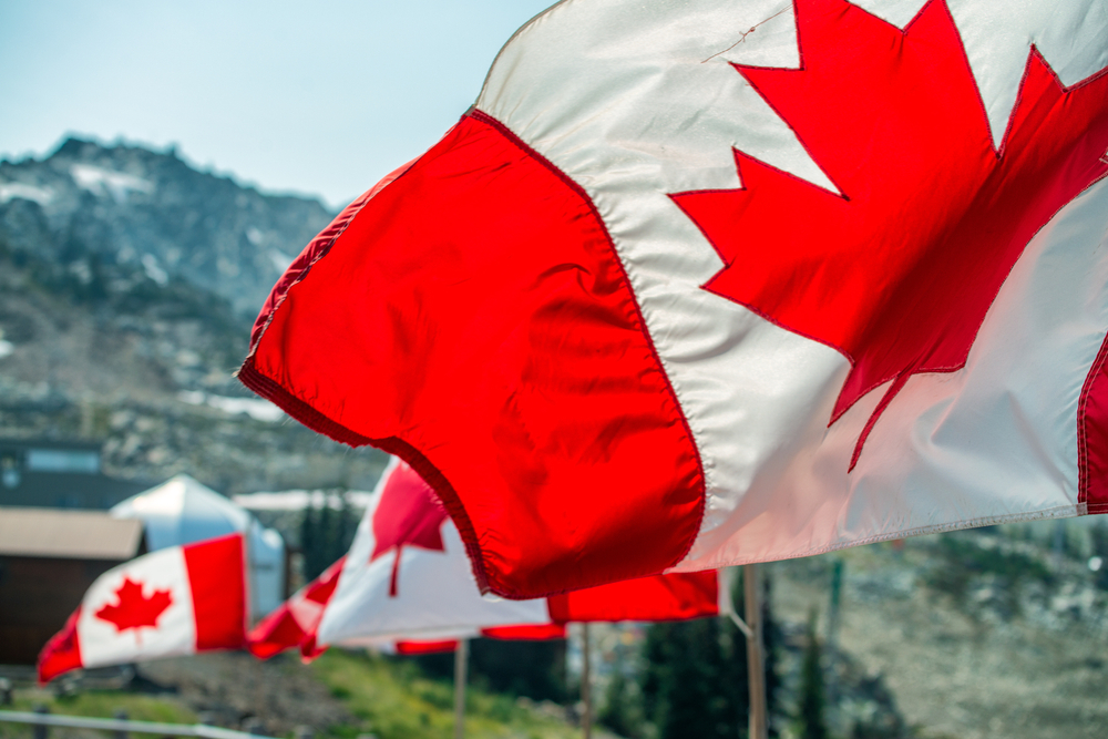 Canada flags waving at the wind in mountain scenario