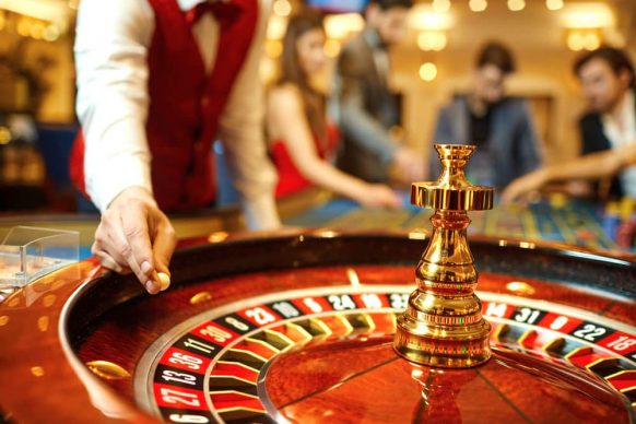 A dealer rolls the roulette ball with players making bets in the background