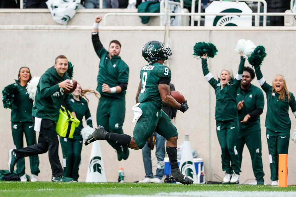 An american football player celebrates a touchdown with the fans and cheerleaders.